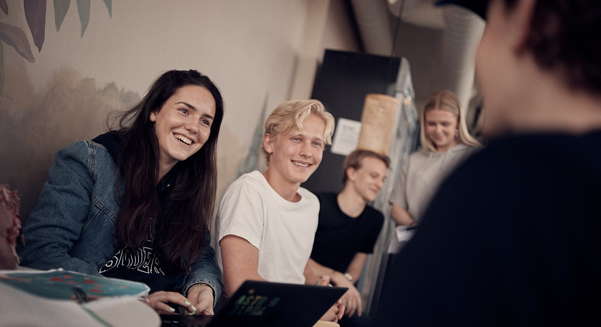 Två elever som sitter i skolans korridor och pratar med sina klasskamrater.